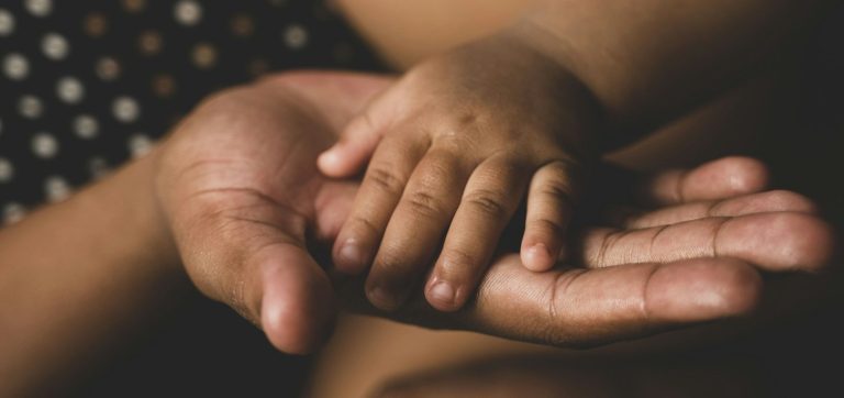 Ein Erwachsener hält die kleine Hand eines Kindes in der eigenen Hand.