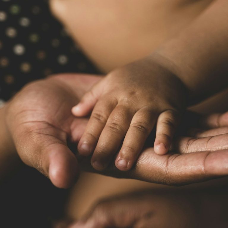 Ein Erwachsener hält die kleine Hand eines Kindes in der eigenen Hand.