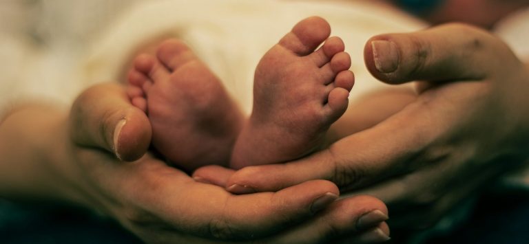 Zwei kleine Babyfüße, gehalten von einer erwachsenen Hand.
