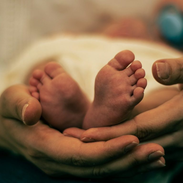 Zwei kleine Babyfüße, gehalten von einer erwachsenen Hand.