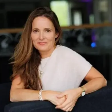 Frau mit langem, lockigem Haar, lächelt, sitzt auf einem Sofa in einem modernen Raum.