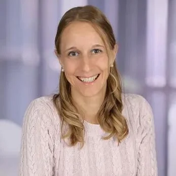 Frau mit blonden Haaren und freundlichem Lächeln, trägt einen hellen Pullover.