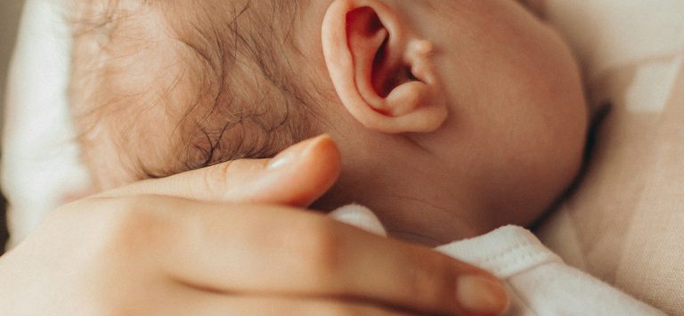 Ein Erwachsener hält sanft einen Kopf eines schlafenden Babys.
