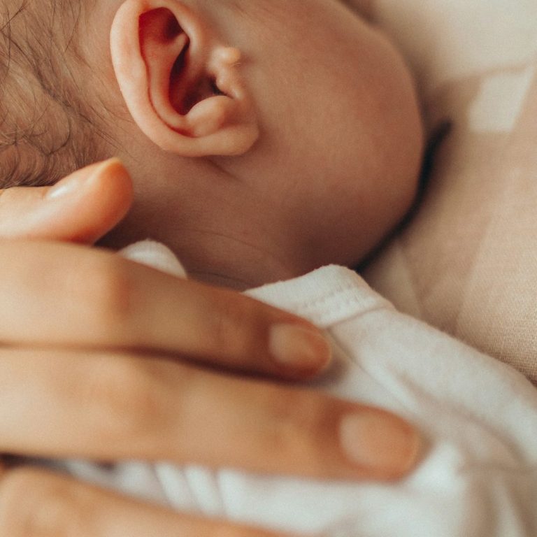 Ein Erwachsener hält sanft einen Kopf eines schlafenden Babys.